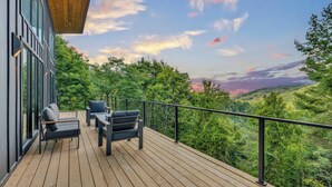 Eine Holzterrasse mit Gartenmöbeln und Blick auf eine bewaldete Landschaft.