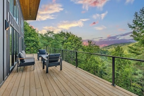 A wooden deck with outdoor furniture and a view of a forested landscape. - New Luxury Cabin - HotTub & Views - 5 min to Boone (Blowing Rock)