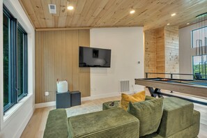 A modern living room with a pool table, green upholstered seating, a flat-screen TV mounted on the wall, and wooden paneling on the walls. - New Luxury Cabin - HotTub & Views - 5 min to Boone (Blowing Rock)