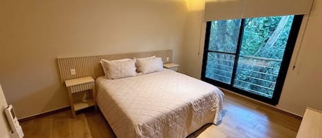 A bedroom with a large bed, a nightstand, a window with a view of trees, and a ceiling light.