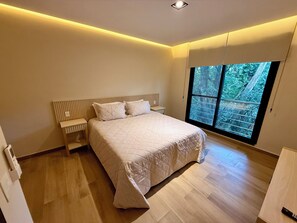 Un dormitorio con una cama grande, una mesita de noche, una ventana con vistas a árboles y una lámpara en el techo.