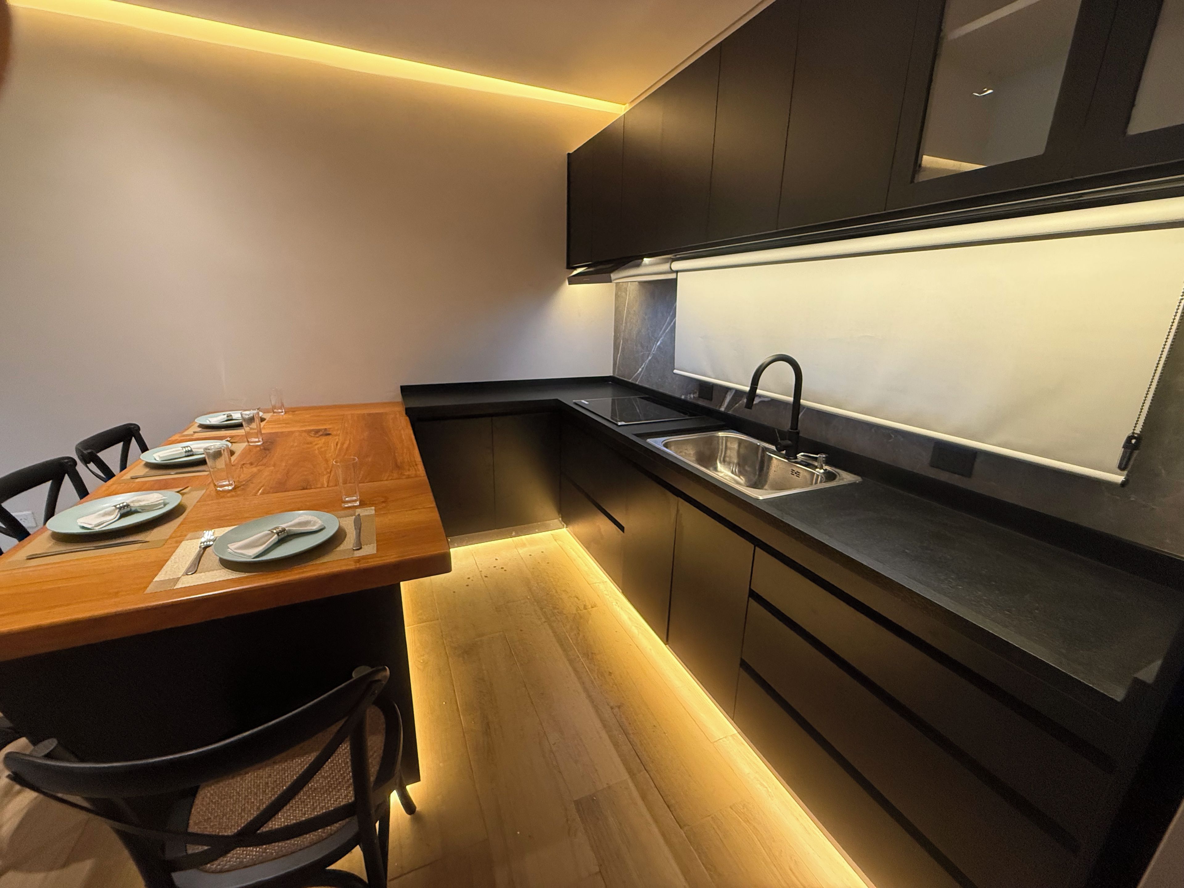 Une cuisine moderne avec une table à manger en bois, des meubles de rangement noirs et un évier en acier inoxydable.