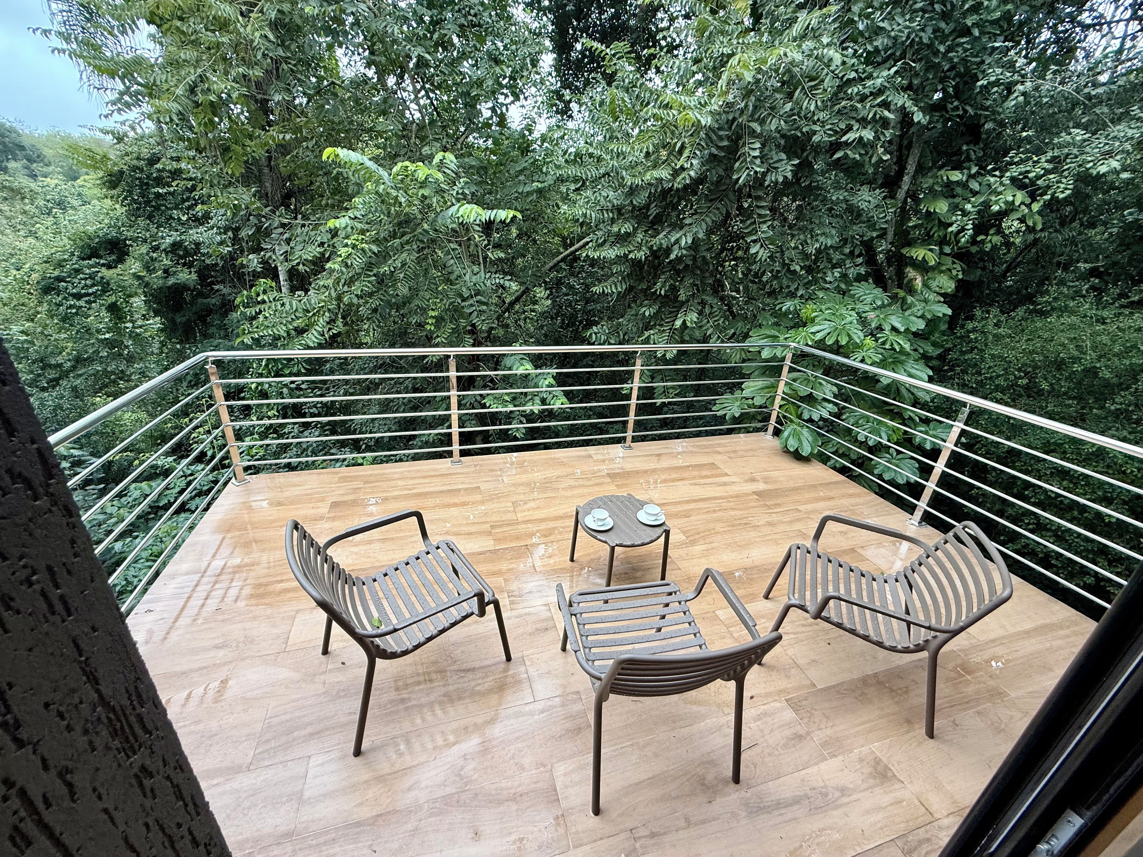 An outdoor deck with a wooden floor, surrounded by metal railings, featuring two chairs and a small round table.