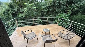 An outdoor deck with a wooden floor, surrounded by metal railings, featuring two chairs and a small round table.