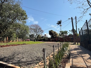 Una calle residencial con entrada de grava, acera y valla metálica.