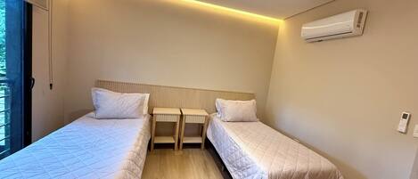A hotel room with two beds, a ceiling light, an air conditioner, and a window.