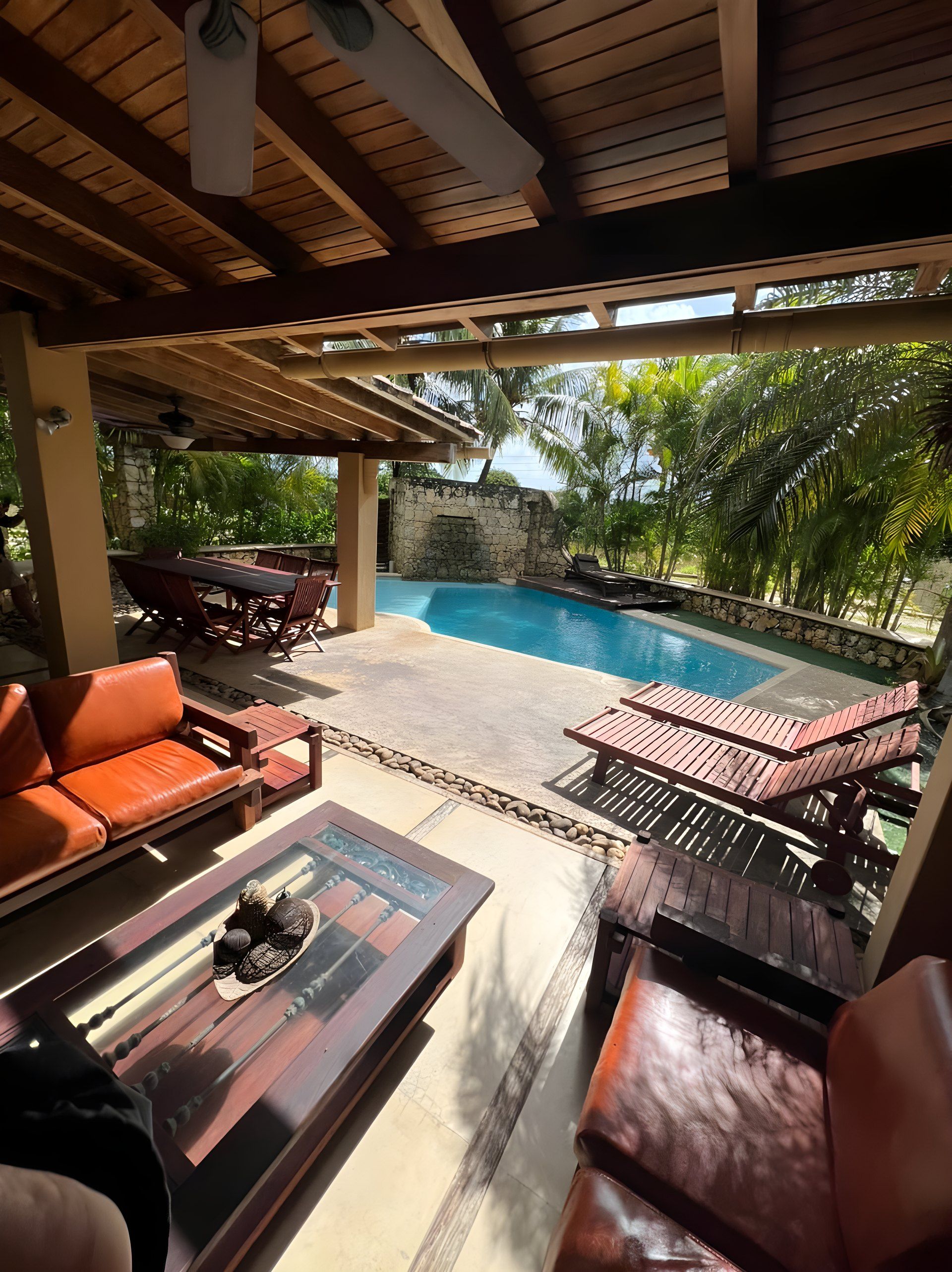 An outdoor seating area with a pool, wooden furniture, and a stone wall.