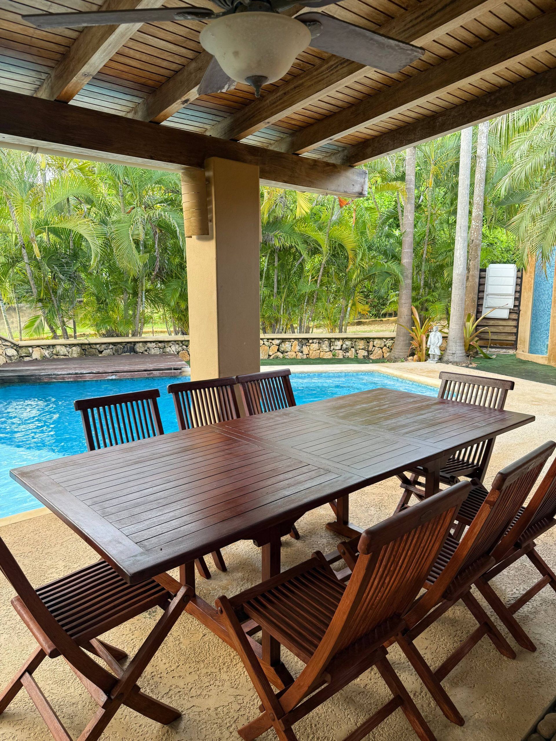 Un espace extérieur abrité, doté d’une piscine, de mobilier en bois et d’une végétation tropicale.