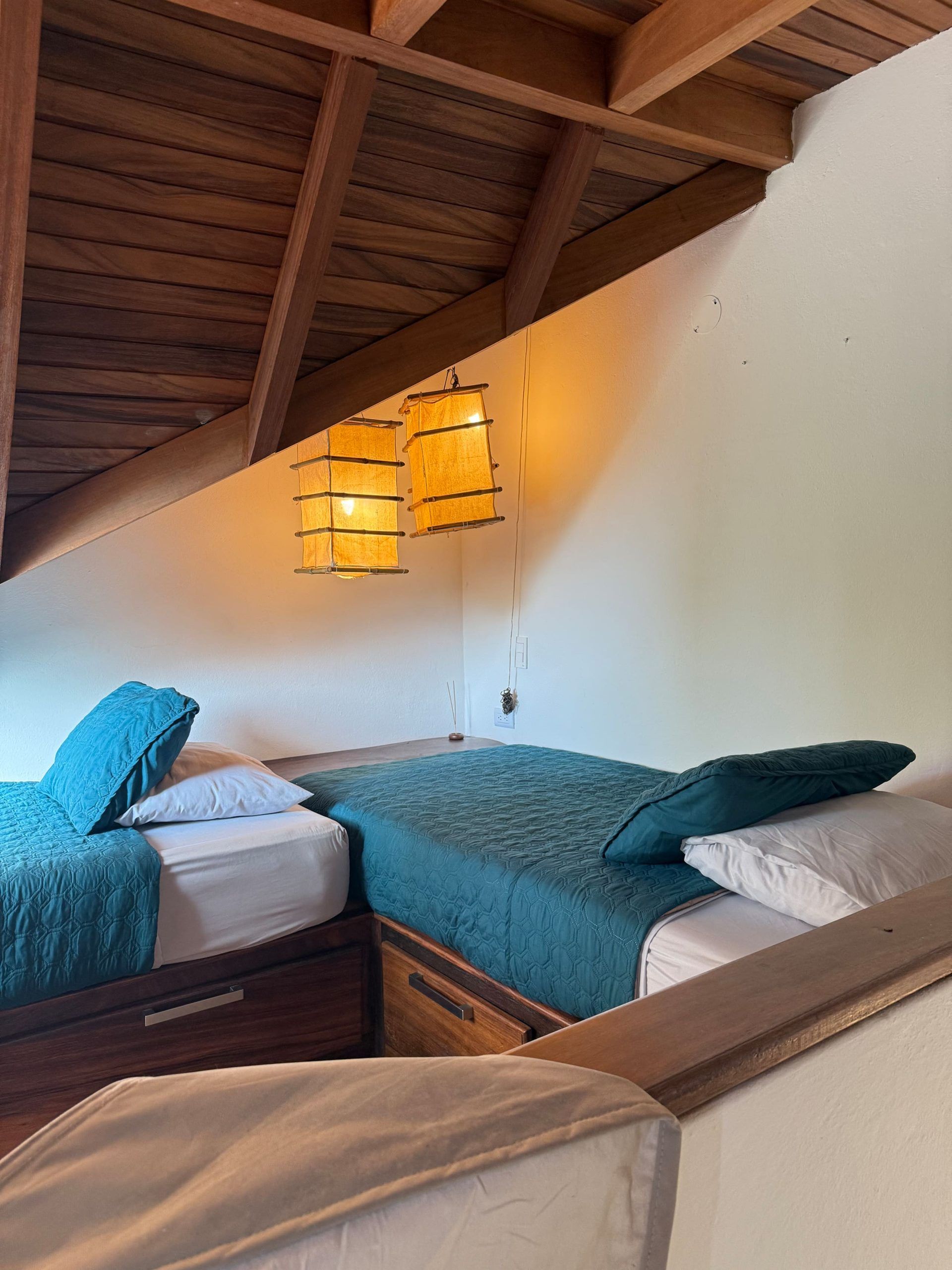 Camera da letto con due letti, travi in legno al soffitto e lampade a sospensione.