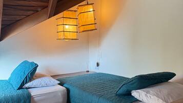Camera da letto con due letti, travi in legno al soffitto e lampade a sospensione.
