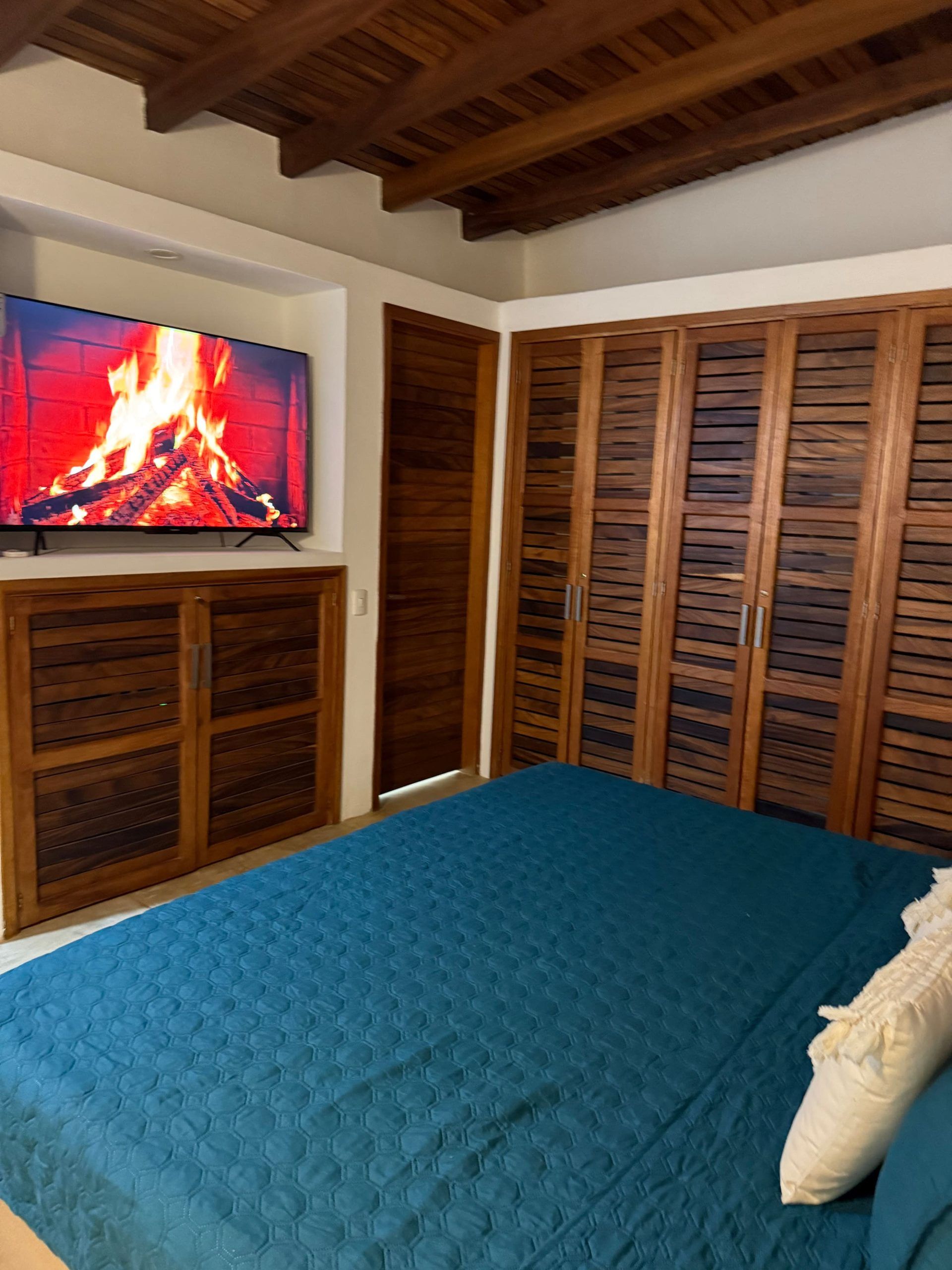 Une chambre à coucher avec un lit, une armoire en bois et un téléviseur diffusant une image de feu.