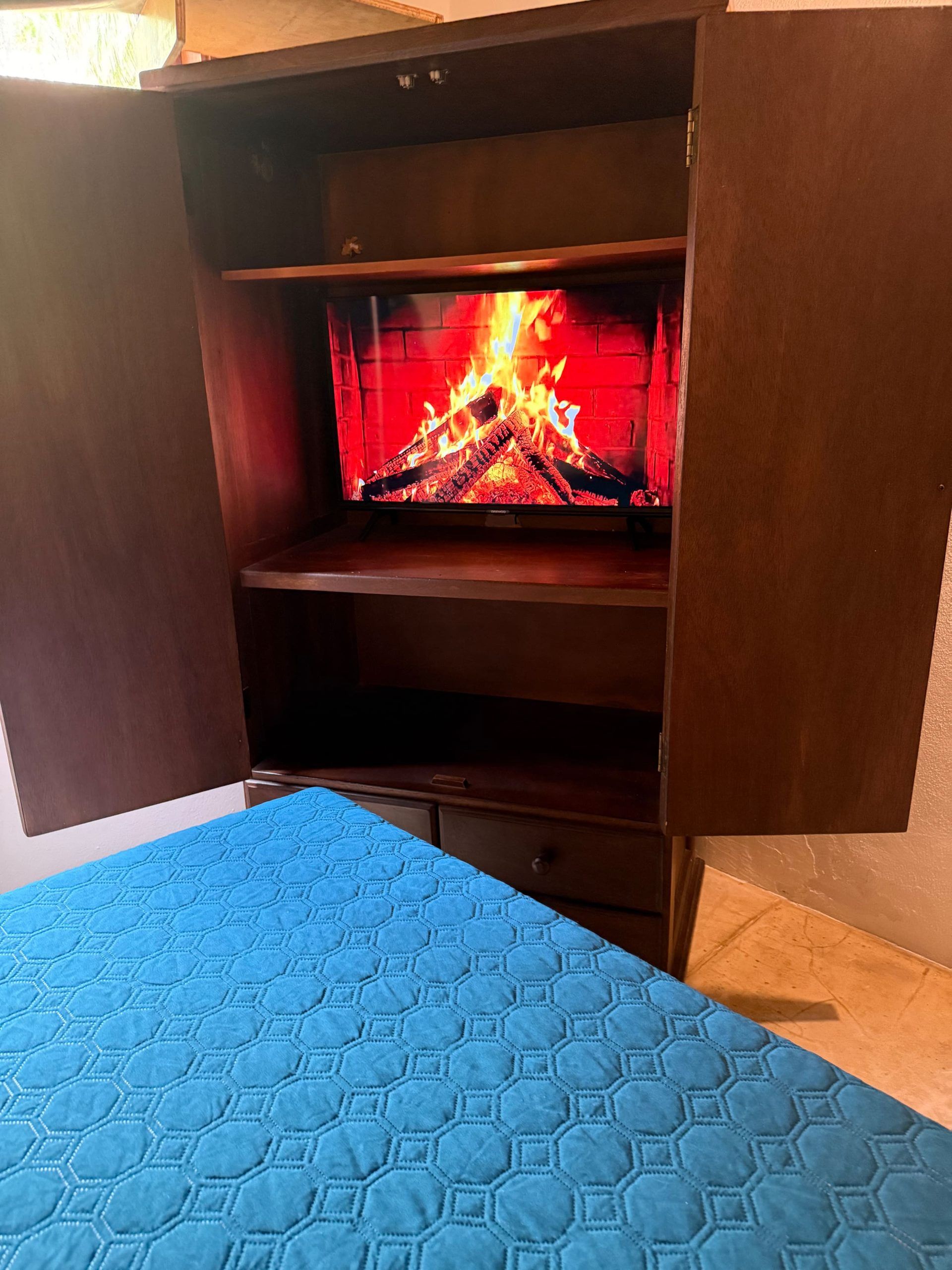Une pièce avec un lit, une armoire en bois et une cheminée où brûle le feu.