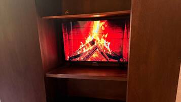 Une pièce avec un lit, une armoire en bois et une cheminée où brûle le feu.