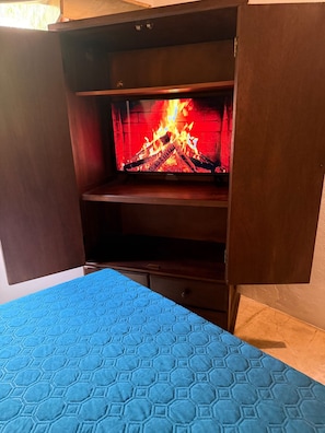 Una habitación con una cama, un armario de madera y una chimenea encendida.