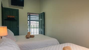 A hotel room with two beds, a television on the wall, and a view of the outside through a door.