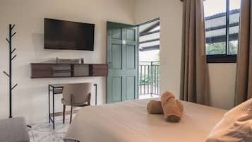 A hotel room with a bed, a desk, a chair, a TV mounted on the wall, and a door leading to an outdoor area.