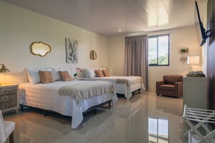 A bedroom with two beds, a sitting area with a chair, and a window with curtains.