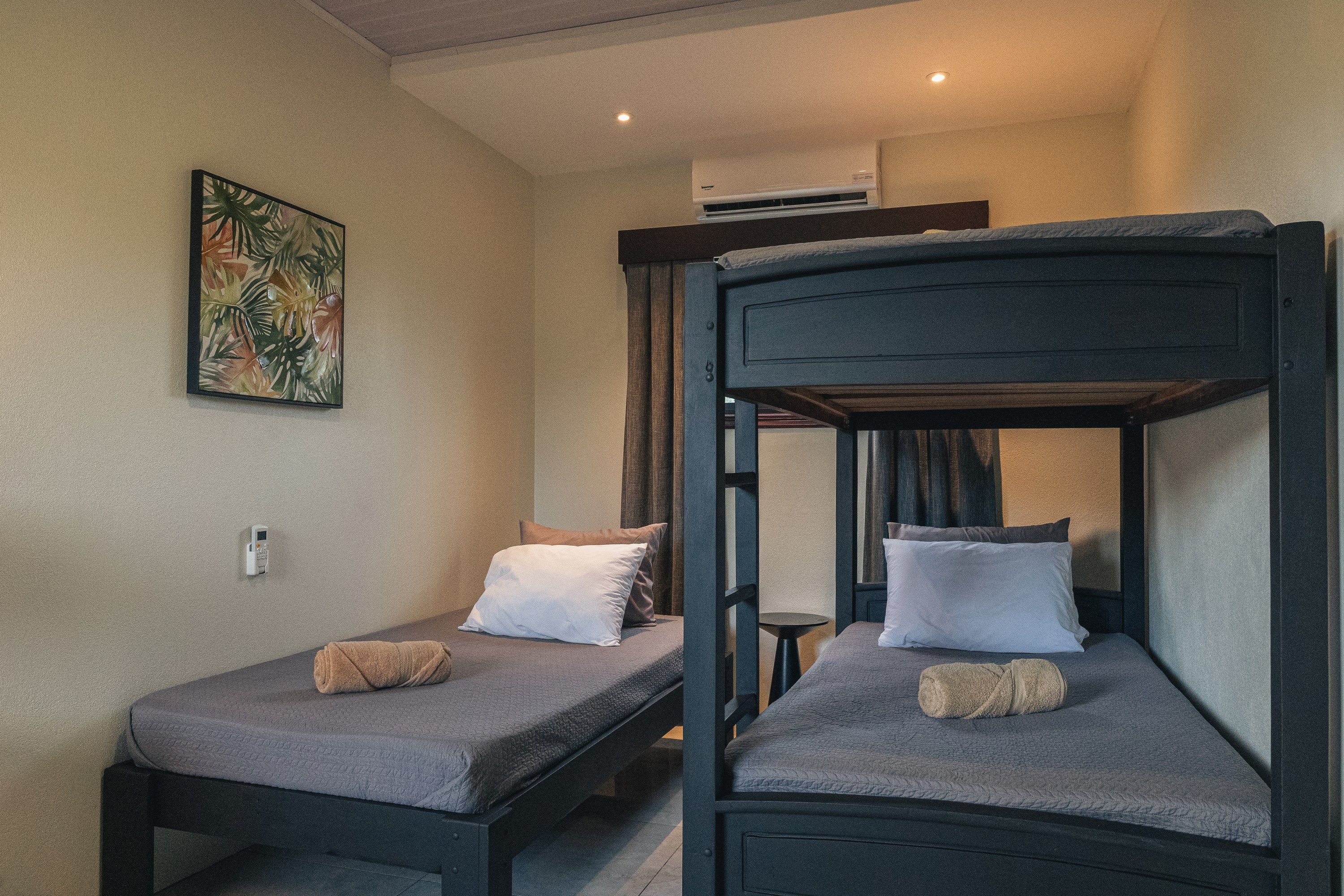 A room with two bunk beds, a small table, a wall-mounted air conditioner, and a painting.