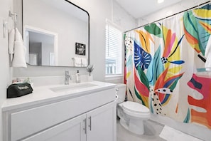 Ein Badezimmer mit einem weißen Waschbecken, einem Spiegel, einer Toilette und einem farbenfrohen Duschvorhang.