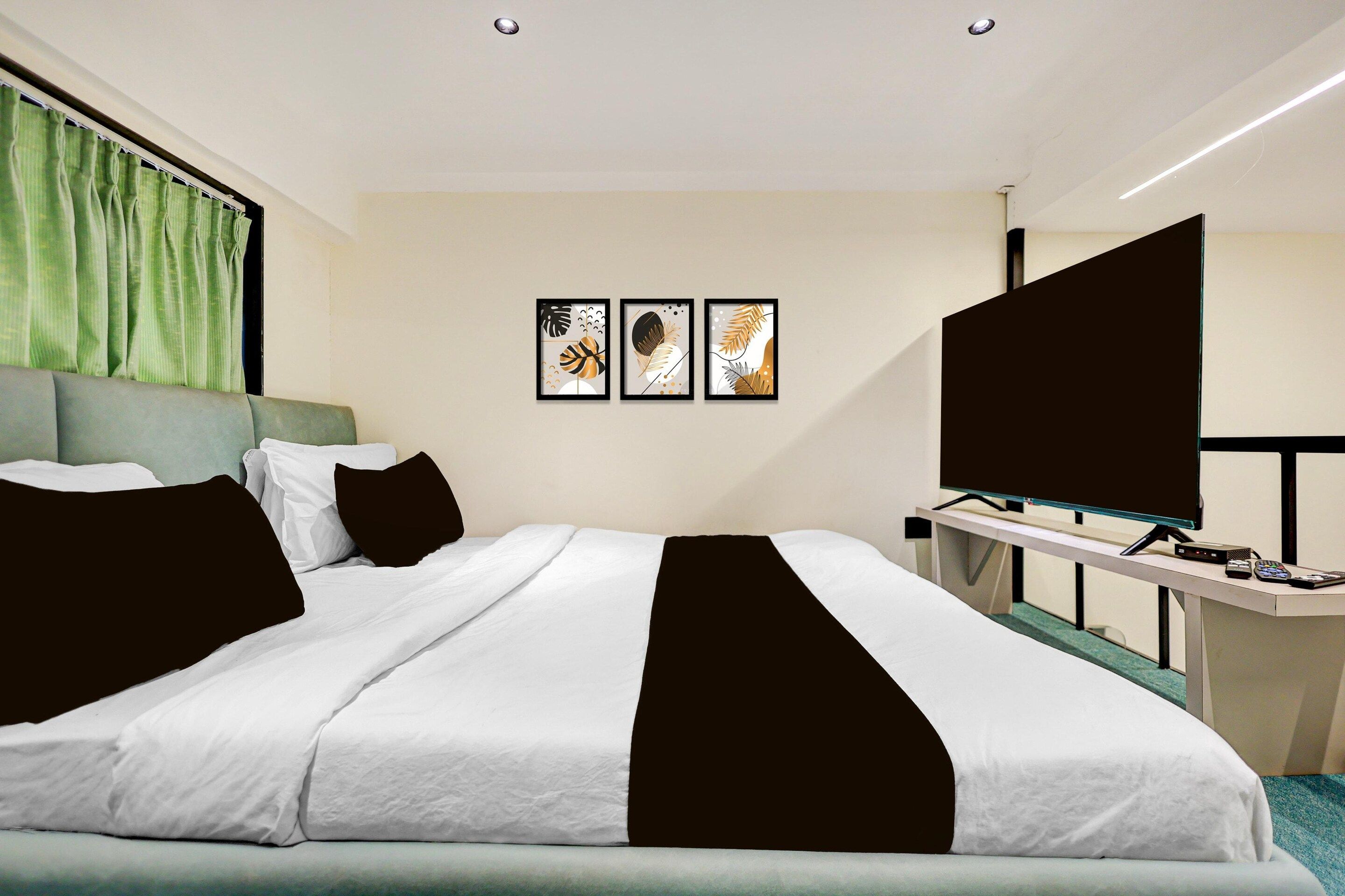 Ein Hotelzimmer mit einem Bett, einem Schreibtisch mit Fernseher und drei gerahmten Kunstwerken an der Wand.