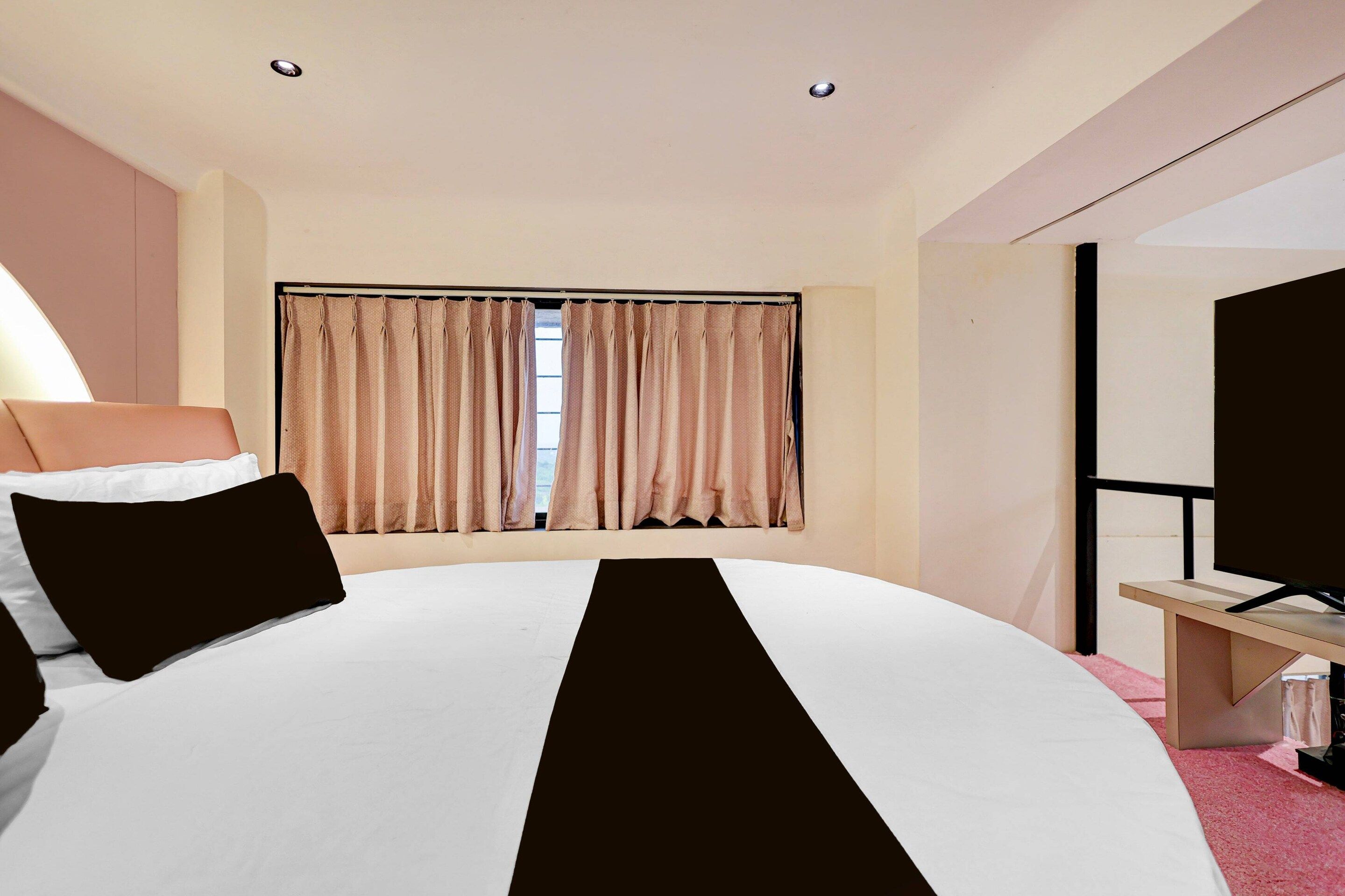 Habitació d'hotel amb un llit gran, televisió, escriptori i finestra amb cortines.