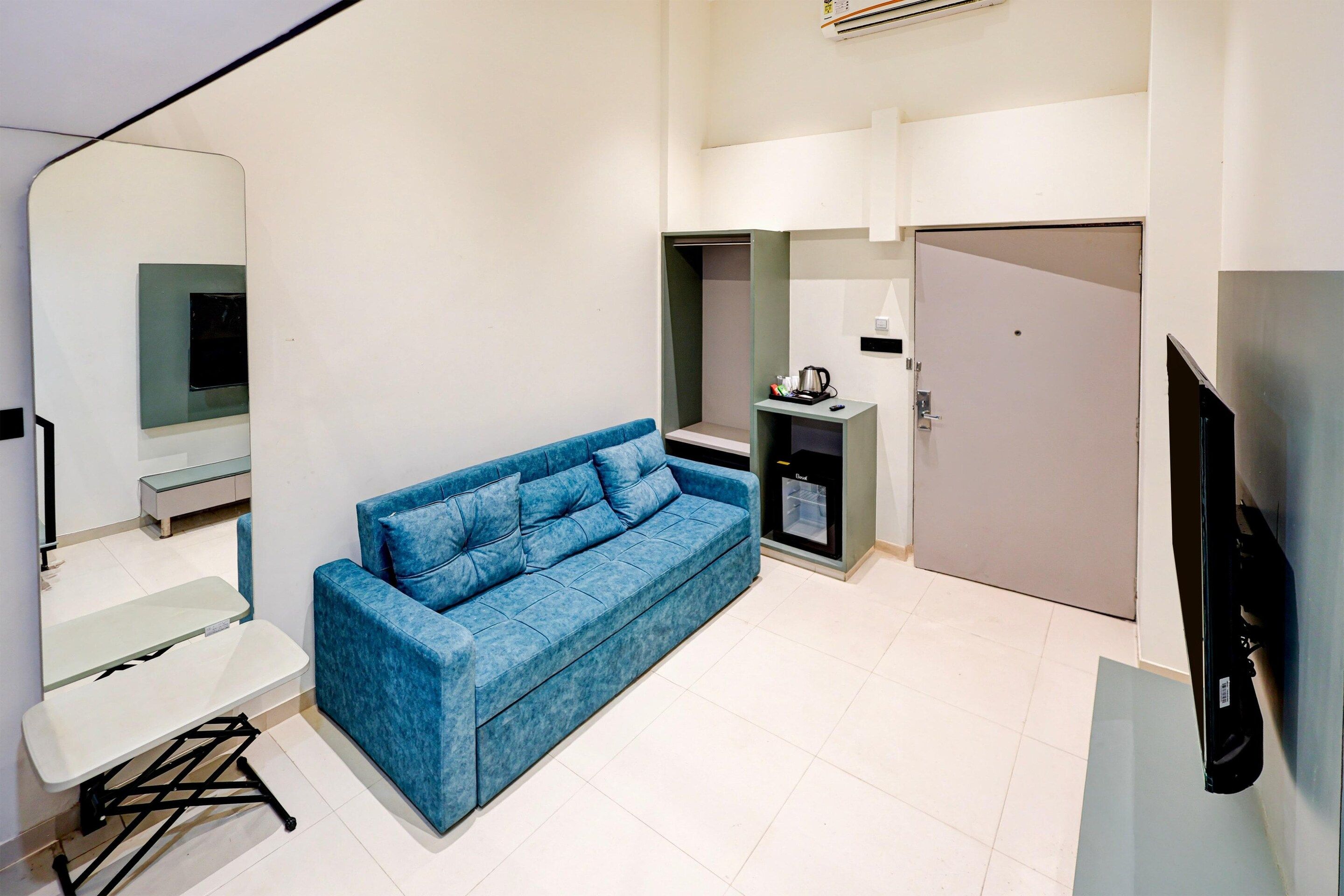Un espacio habitable compacto con un sofá azul, una mesa pequeña, una kitchenette con cafetera y un televisor.