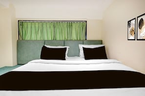 A bedroom with a bed, green curtains, and two framed artworks on the wall.