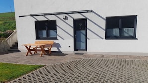 Un edificio moderno con facciata bianca, due finestre, un ingresso e una panchina di legno all'esterno.