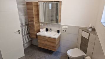 Ein Badezimmer mit Toilette, einem Holzbidet mit Spiegel, einem Waschbecken und einem Handtuch.