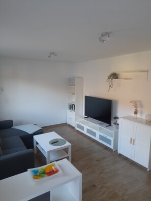 Una sala de estar moderna con una televisión de pantalla plana, un sofá, una mesa de centro y estanterías empotradas.