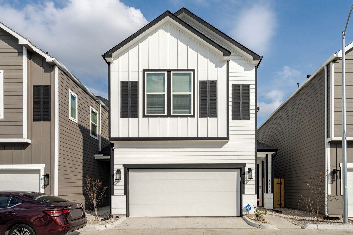 A two-story residential building with a garage, a driveway, and a parked car.