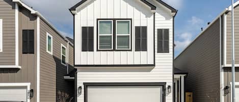 A two-story residential building with a garage, a driveway, and a parked car.