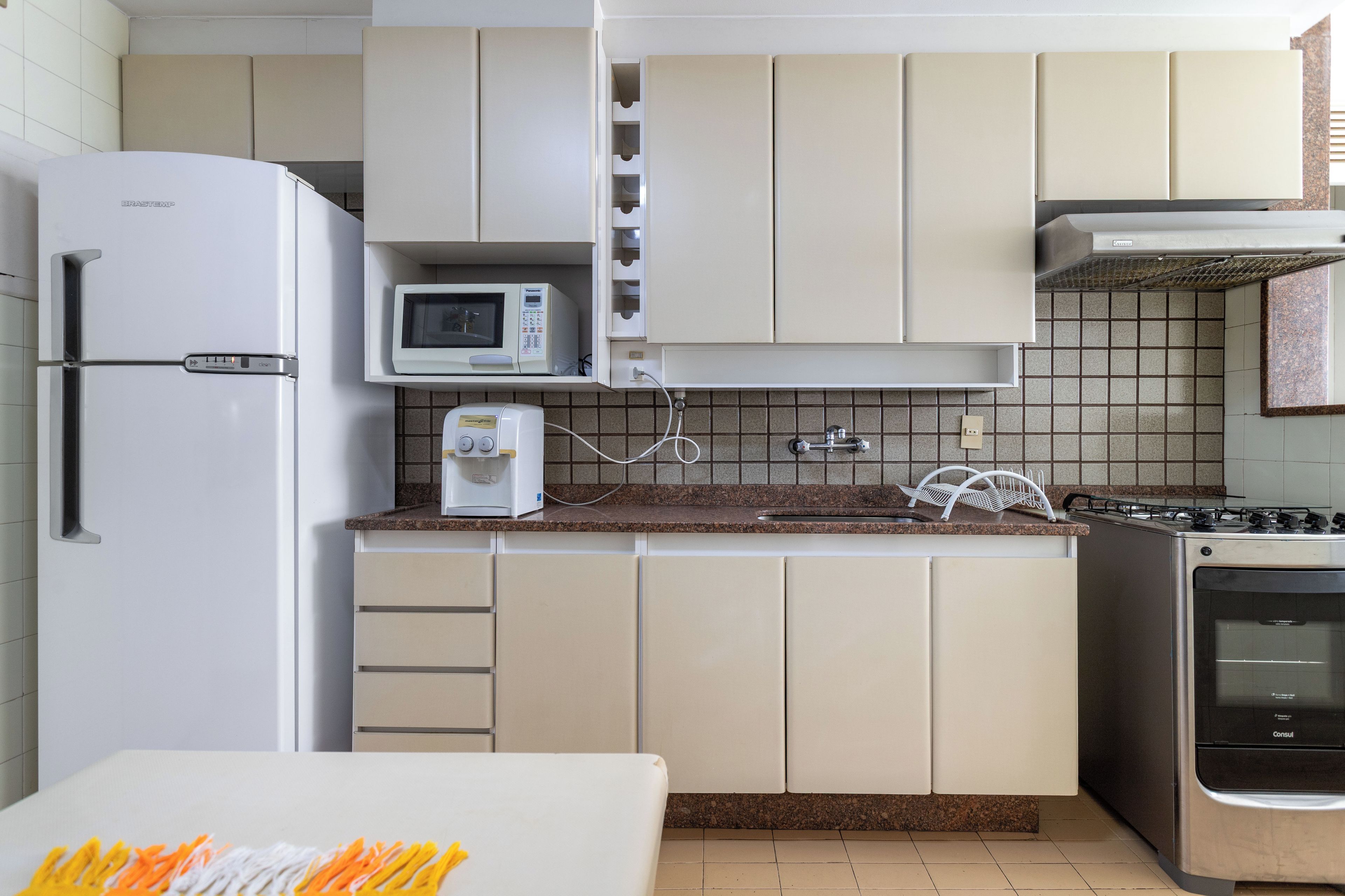 Una cucina compatta con frigorifero, microonde, macchina del caffè e fornello.