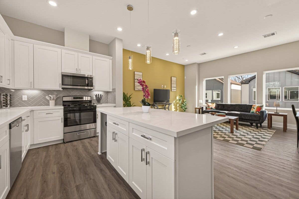 A modern kitchen with white cabinetry, a central island, and a dining area with a sofa and coffee table.