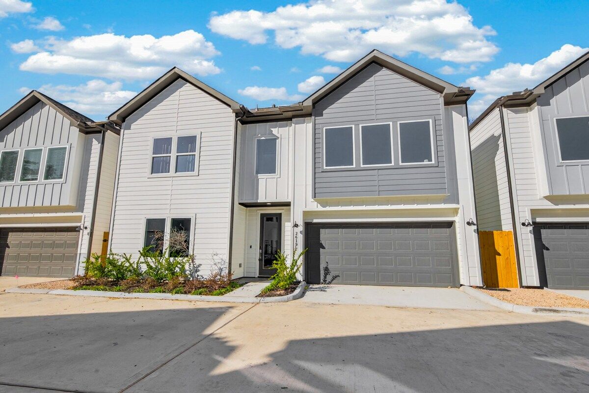 A row of townhouses with attached garages, a front yard with landscaping, and a clear sky.