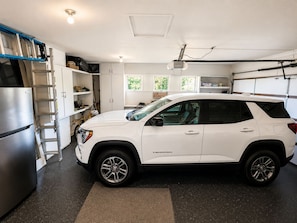 A white SUV in a garage with a kitchen area, a ladder, and a sign for an auto body shop. - Beautiful Home in Quiet Gated Community Near Hendry's Beach-3Bedrooms 2.5 Baths (Santa Barbara)