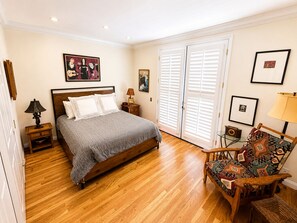 A bedroom with a wooden bed, a chair with a patterned cushion, a nightstand with a lamp, and a door with white shutters. - Beautiful Home in Quiet Gated Community Near Hendry's Beach-3Bedrooms 2.5 Baths (Santa Barbara)