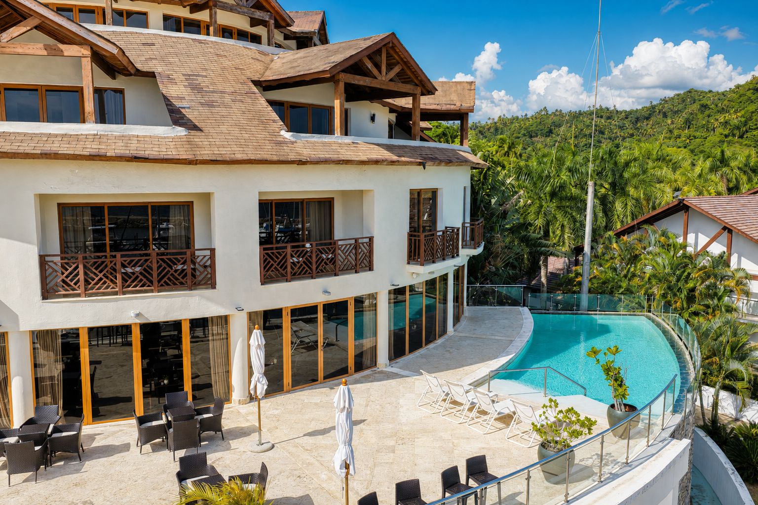 Un hotel de varios pisos con piscina, zona de estar exterior y vistas a un paisaje tropical.