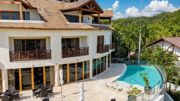 Un hotel de varios pisos con piscina, zona de estar exterior y vistas a un paisaje tropical.