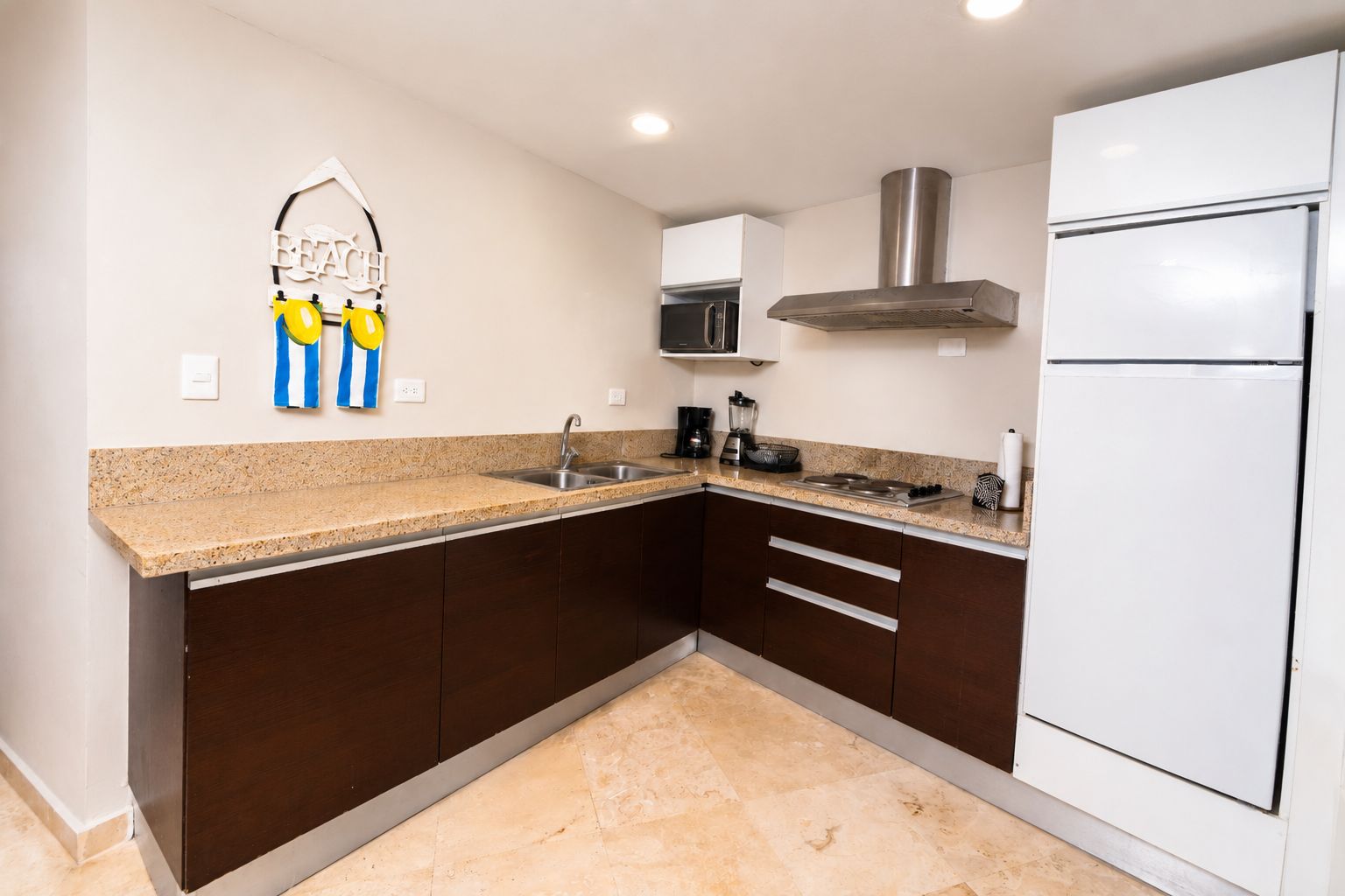 Una cocina con gabinetes marrón oscuro, encimera de granito, extractor de acero inoxidable, microondas y refrigerador blanco.