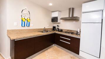 Una cocina con gabinetes marrón oscuro, encimera de granito, extractor de acero inoxidable, microondas y refrigerador blanco.