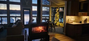 A cozy interior with a fireplace, dining area, and large windows overlooking a body of water.