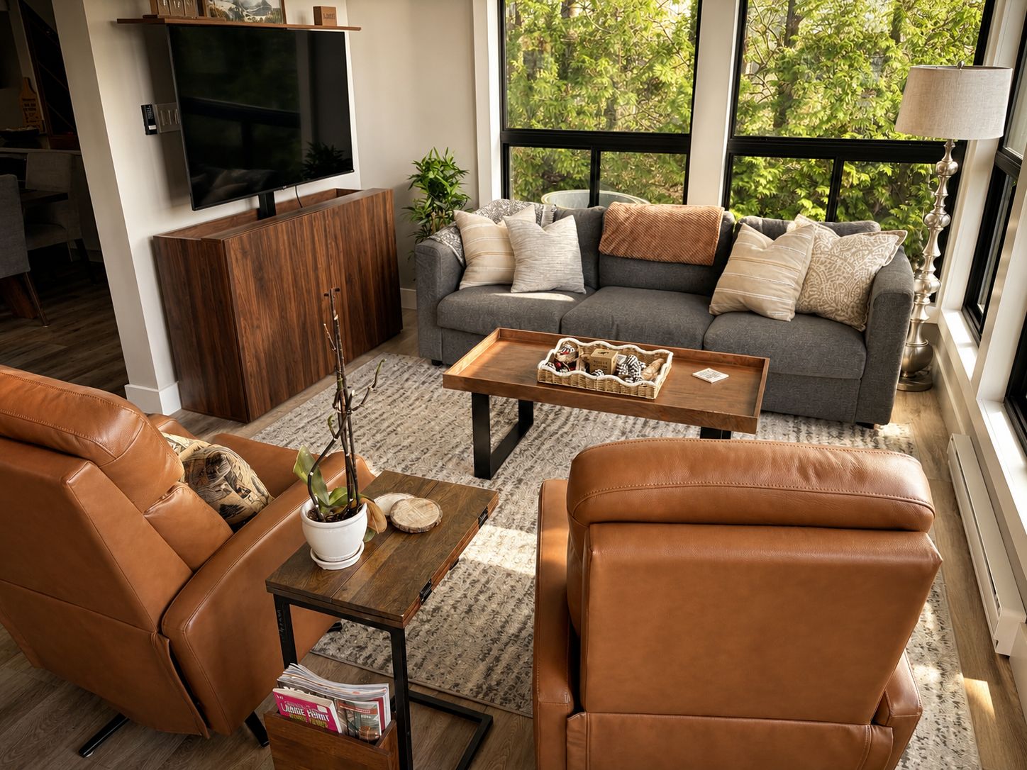 A modern living room with leather furniture, a flat-screen TV, and a large window with a view of trees.