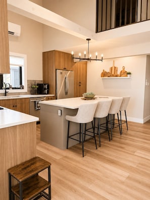 A modern kitchen with a central island, wooden cabinets, a stainless steel refrigerator, and a hanging light fixture.