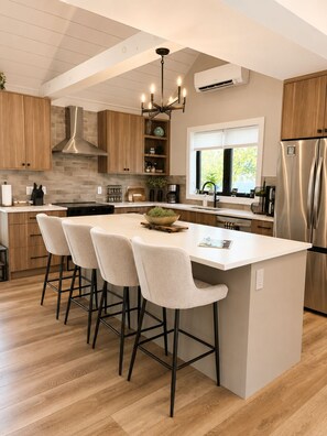 A modern kitchen with a central island, bar stools, a stainless steel refrigerator, and a window providing natural light.