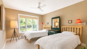 Une chambre avec deux lits, un ventilateur de plafond, une fenêtre avec vue et une lampe.