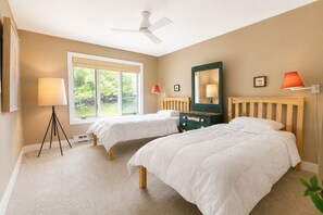 Een slaapkamer met twee bedden, een plafondventilator, een raam met uitzicht en een lamp.