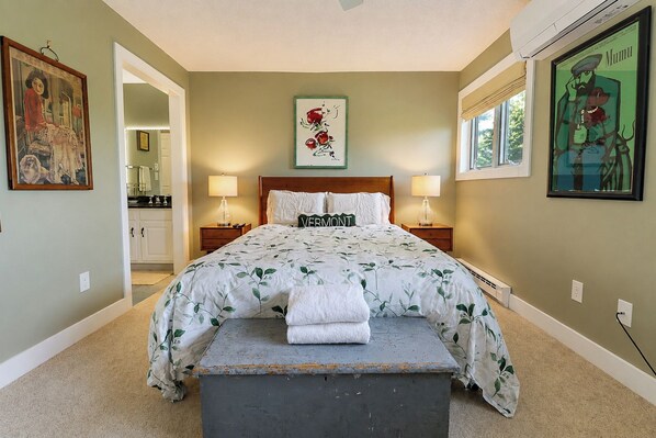 A bedroom with a bed, two bedside tables, a nightstand, a bench, and artwork on the walls.