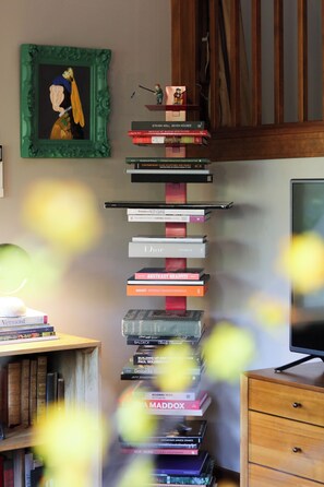 A room with a bookshelf filled with various books, a framed picture on the wall, and a television on a wooden cabinet.