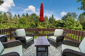 An outdoor patio with wicker furniture, a wooden table, and a red umbrella.